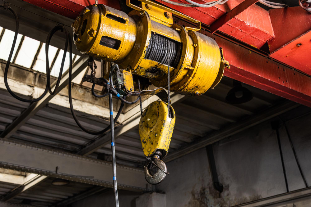 Industrial electric chain hoist lifting heavy cargo in a Malaysian warehouse.